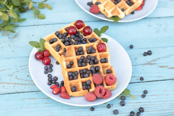 Национальный день вафель. Вафли со смесью ягод на деревянном голубом фоне в голубой тарелке . — стоковое фото