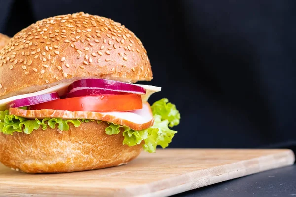 Burger with meat cheese tomato onions on a board on a black background copy space — Stock Photo, Image