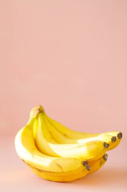 Sarı muzlar pembe arka planda yatar. Güneş ışığında bir avuç muz.
