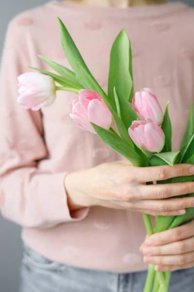 pink tulips with green leaves in a glass vase, a woman holding tulips in her hands