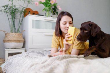 Genç ve güzel beyaz saçlı bir kadın siyah saçlı bir selfie çekip köpeğiyle yatağa uzanır.
