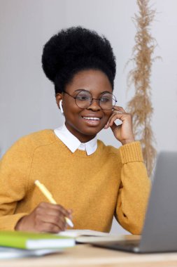 Millennial Afro-Amerikan kadın sarı kazaklı ve afro saçlı ev ofisinde çalışıyor.