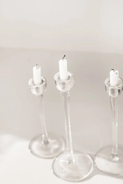 Velas blancas en candelabros de vidrio sobre fondo blanco, diseño interior o decoración — Foto de Stock