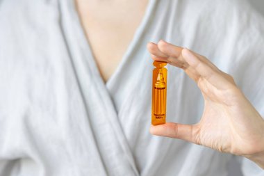 Beyaz kadın elinde saç ve deri için vitamin ampulleri tutuyor.