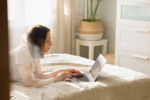 Καυκάσια γυναίκα στο γραφείο δακτυλογράφησης στο φορητό υπολογιστή ξαπλωμένη στο κρεβάτι — Φωτογραφία Αρχείου