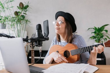 Podcast, müzik içeriği oluşturma. Güzel Avrupalı kadın podcaster, gitar ya da ukulele şapkalı, radyo sunucusu podcast veya içerik kaydediyor, şarkı ve müzik bir kayıt stüdyosunda