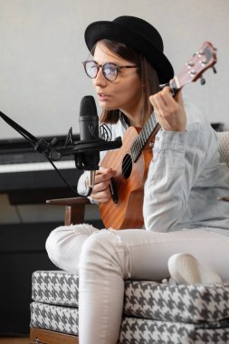 podcast, music audio content creation. beautiful European woman podcaster in a hat with a guitar or ukulele, radio host recording podcast or content