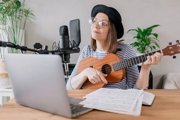 Podcast, creación de contenido de audio musical. hermosa mujer europea podcaster en un sombrero con una guitarra o ukelele, radio anfitrión grabación podcast o contenido, canción y música en un estudio de grabación — Foto de Stock