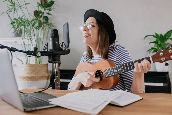 Podcast, criação de conteúdo de áudio de música. bela mulher europeia podcaster em um chapéu com uma guitarra ou ukulele, rádio anfitrião gravação podcast ou conteúdo, música e música em um estúdio de gravação — Fotografia de Stock