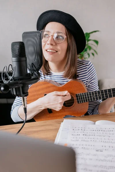Podcast, criação de conteúdo de áudio de música. bela mulher europeia podcaster em um chapéu com uma guitarra ou ukulele, rádio anfitrião gravação podcast ou conteúdo, música e música em um estúdio de gravação — Fotografia de Stock