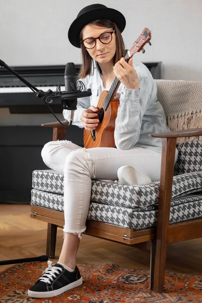 Podcast, music audio content creation. beautiful European woman podcaster in a hat with a guitar or ukulele, radio host recording podcast or content — Foto de Stock