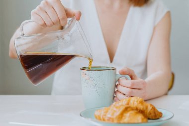 Avrupalı bir kadın mutfakta kahve yapıyor ve sabah keyfine bakıyor. Beyaz bir kadın evde kahve filtresi yapıyor ve izin gününün tadını çıkarıyor.