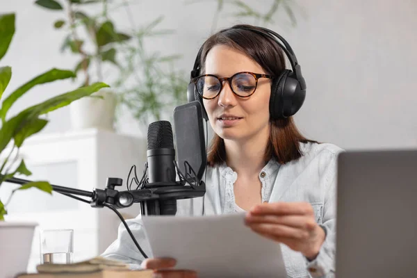 the stylish and educated caucasian woman records podcasts in a recording studio or in her home. the European millennial woman creates audio content or records text, records an audio book or radio show
