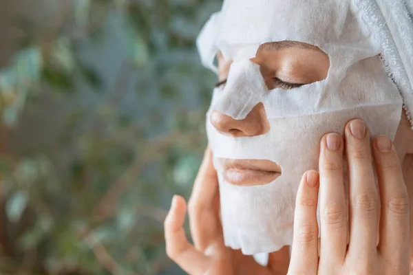Európai nő alkalmazza fehér ruha hidratáló maszk az arcára, arc bőrápoló és spa kezelések otthon, nő kozmetikus csinál anti-aging arc maszk — Stock Fotó