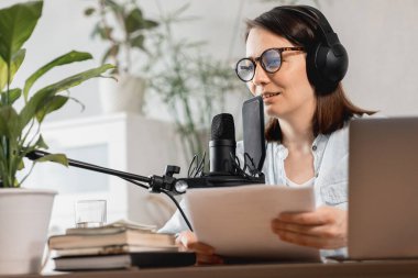 Podcaster içerik yaratır, Avrupalı kadın mikrofon ve kulaklıkla podcast kaydeder, beyaz kadın reklam veya ses kitabı için ses kaydı yapar