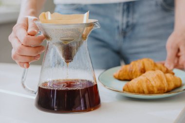  Sabahları kahve, kahve yapan ve içen Avrupalı bir kadın. Kahvaltıda kruvasan ve kahve.