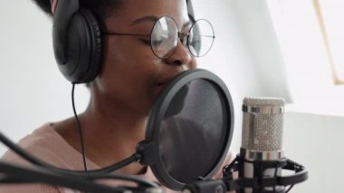 Podcast ve ses içeriği oluşturma, özgüvenli ve güzel bir Afrikalı-Amerikalı kadın mikrofon ve kulaklıkla bir kayıt stüdyosunda veya evinde podcast kaydediyor.
