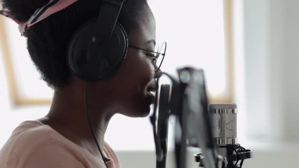 Podcast en audio content creatie, zelfverzekerde en mooie Afro-Amerikaanse vrouw met een microfoon en een koptelefoon die een podcast opneemt in een opnamestudio of in haar huis — Stockvideo
