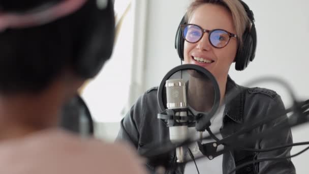 Une femme européenne avec casque parle dans un microphone, deux femmes dans un studio d'enregistrement créent du contenu audio — Video