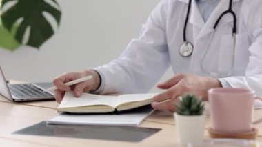 Tıp kliniğindeki ofisinde beyaz önlüklü bir doktor günlüğüne bir yazı yazar. Bir doktor hastalarını bilgisayarında muayene ettikten sonra çalışır.,