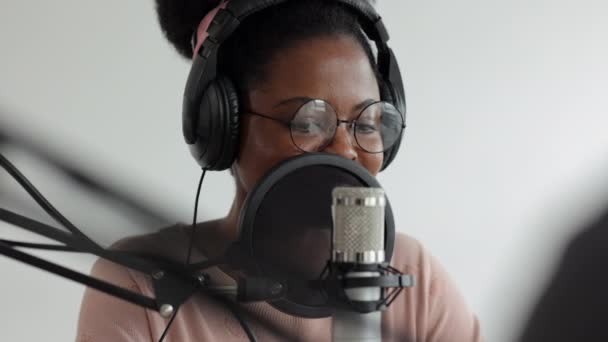 Creación de contenido de podcast y audio, mujer afroamericana segura y hermosa con un micrófono y auriculares grabando un podcast en un estudio de grabación o en su casa — Vídeos de Stock