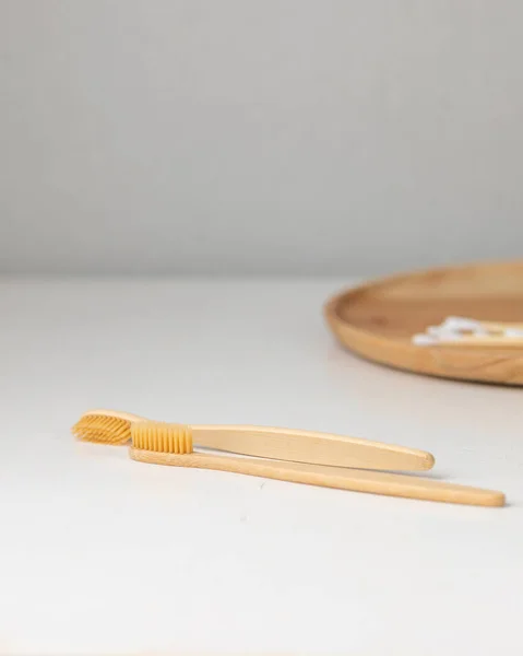 Daily human hygiene, cotton swabs and cotton pads, a womans hand holding bamboo toothbrushes on a light background in a glass or against the background of a wooden tray — Stock Photo, Image