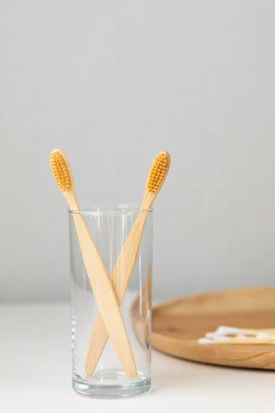 Daily human hygiene, cotton swabs and cotton pads, a womans hand holding bamboo toothbrushes on a light background in a glass or against the background of a wooden tray — Stock Photo, Image