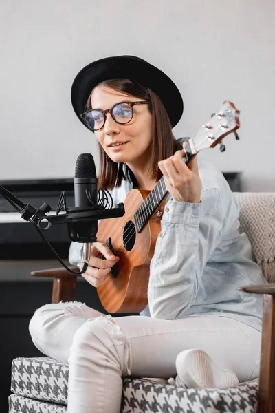 Podcaster crea contenido, mujer feliz músico con grabaciones de guitarra podcast con micrófono y auriculares, mujer caucásica en gafas y sombrero — Foto de Stock