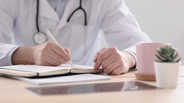 Lékař v bílém plášti ve své kanceláři na lékařské klinice si zapíše do deníku, lékař pracuje poté, co navštívil pacienty u počítače, — Stock video