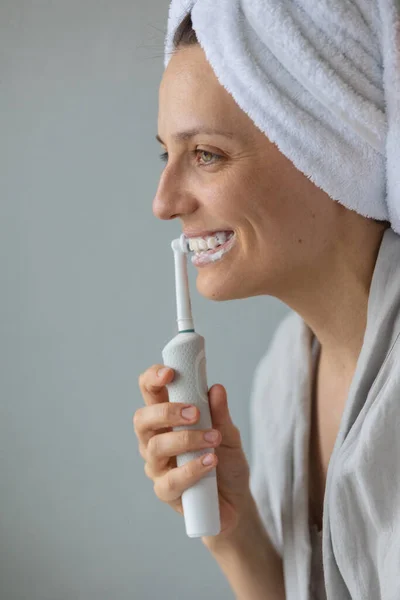 Avrupalı bir kadın dişlerini elektrikli diş fırçası, ağız ve diş bakımı, insan kişisel hijyeni, diş macunu ile güçlendirip beyazlatıyor. — Stok fotoğraf