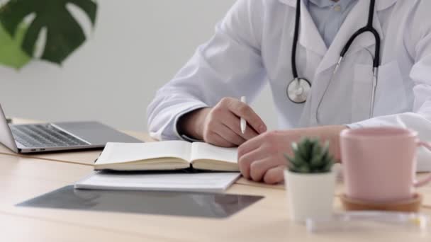 Un médico con una bata blanca en su consultorio en una clínica médica hace una entrada en su diario, un médico trabaja después de ver a los pacientes en una computadora, — Vídeos de Stock
