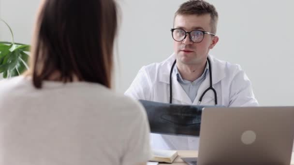 Médico con una bata blanca y gafas hablando con su paciente en un consultorio o clínica del hospital — Vídeos de Stock