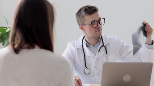 하얀 외투를 입고 안경을 쓴 의사 가 병원 사무실이나 진료소에서 환자에게 이야기하는 모습 — 비디오