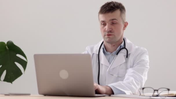 Telemedicina, un médico europeo con una bata blanca y gafas hace una nota en un diario y una anotación en un cuaderno — Vídeos de Stock