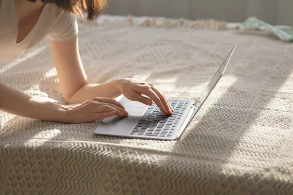 Καυκάσια γυναίκα στο γραφείο στο σπίτι δακτυλογράφηση σε φορητό υπολογιστή που βρίσκεται στο κρεβάτι, ηλιόλουστη μέρα, κατ 'οίκον διδασκαλία — Φωτογραφία Αρχείου