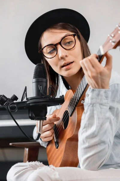 Podcaster crea contenido, mujer feliz músico con grabaciones de guitarra podcast con micrófono y auriculares, mujer caucásica en gafas y sombrero — Foto de Stock