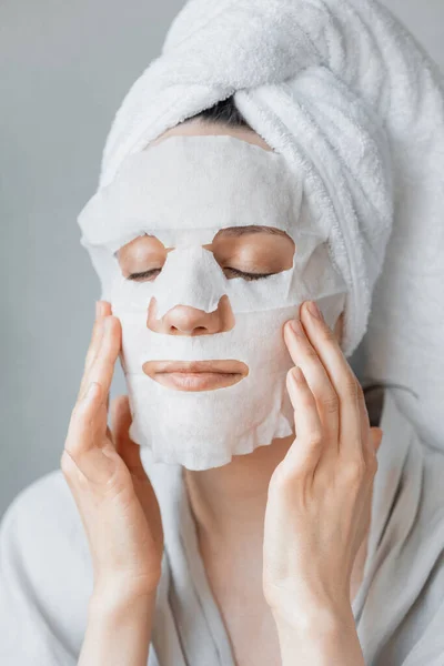 Európai nő alkalmazza fehér ruha hidratáló maszk az arcára, arc bőrápoló és spa kezelések otthon, nő kozmetikus csinál anti-aging arc maszk — Stock Fotó