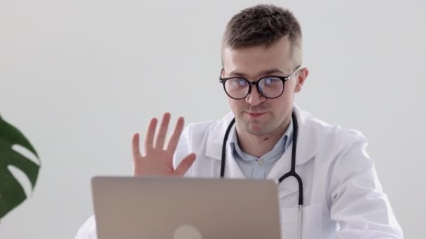 Médico europeo en una clínica hablando con un paciente a través de un enlace de vídeo, un médico caucásico en un consultorio en un hospital diagnostica a un paciente a través de una webcam — Vídeos de Stock