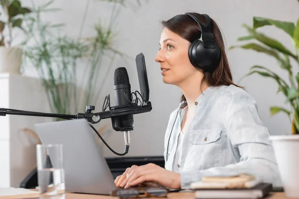 podcaster creates content, European woman records podcast with microphone and headphones, Caucasian woman in recording studio records voice for commercials or audio book