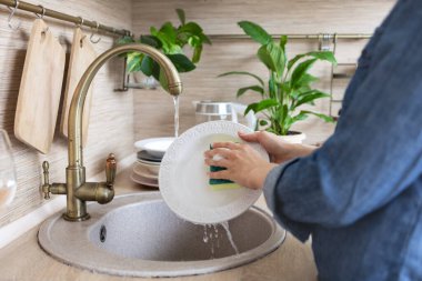 Kadınların elleri mutfak lavabosunda bulaşık yıkar, kadın mutfağı temizler, bulaşıkları yıkar, bulaşık deterjanı köpüğüyle tabakları yıkar, ev temizliği yapar.