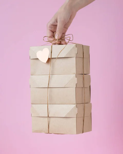 womans hand holding a kraft cardboard box natural color, woman holding boxes with yellow gift ribbon or wrapping. gift or food delivery