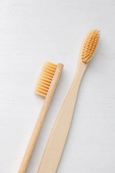 Hygiène humaine quotidienne, coton-tige et tampons de coton, une main de femme tenant des brosses à dents en bambou sur un fond clair dans un verre ou sur le fond d'un plateau en bois — Photo
