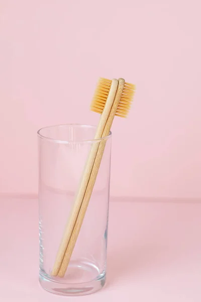 Daily human hygiene, cotton swabs and cotton pads, a womans hand holding bamboo toothbrushes on a pink background in a glass or against a background of plants — Stock Photo, Image