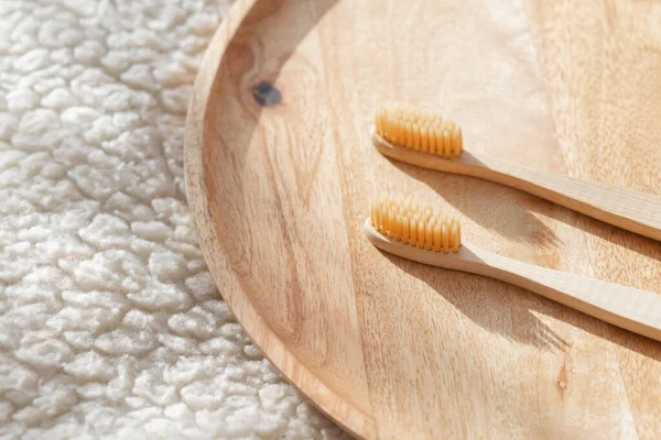 Higiene humana diária, esfregaços de algodão e almofadas de algodão, uma mão de mulher segurando escovas de dentes de bambu em um fundo leve em um copo ou no fundo de uma bandeja de madeira — Fotografia de Stock