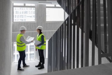 İki mühendis, bir erkek ve bir kadın beyaz kasklı ve yeşil yelekli.