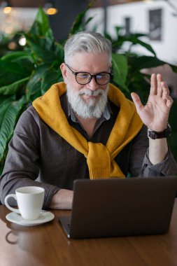 50 yaşında yakışıklı bir adam laptopta çalışıyor ya da video konferansında sohbet ediyor.