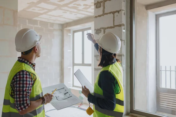 two engineers, a man and a woman in white helmets and green protective vests