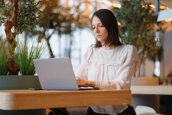 the beautiful and young european woman works on her laptop in a coffee shop or public place