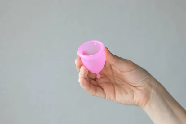 Uma mulher europeia segura uma xícara menstrual rosa feita de silicone em suas mãos — Fotografia de Stock