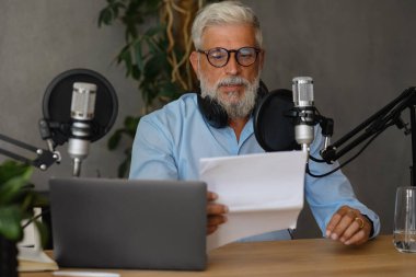 Yaşlı bir adam ses içeriğini kaydeder ya da bir kayıt stüdyosunda radyo programı yönetir. Stüdyoda kulaklığı ve mikrofonu olan gri saçlı ve sakallı bir adam var. 